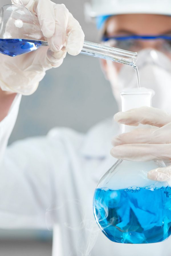 Selective focus on flasks in the hands of a professional female scientist mixing chemicals during experiment at her lab work worker science research profession danger medicine biology reaction concept.